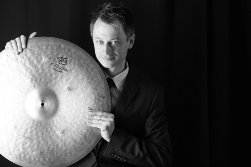 Dennis Frehse holding a cymbal in front of a black background.